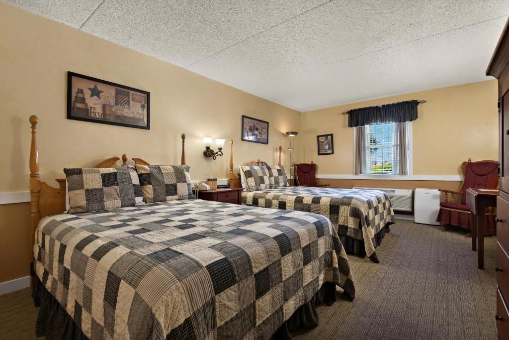 A hotel room with two beds, a desk, a chair, a window with curtains, and wall-mounted lamps.