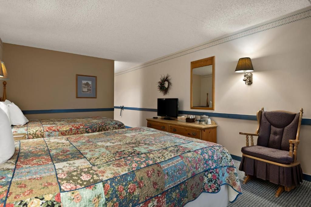 Habitació d'hotel amb dos llits, un taulell, una televisió, una cadira i un mirall.