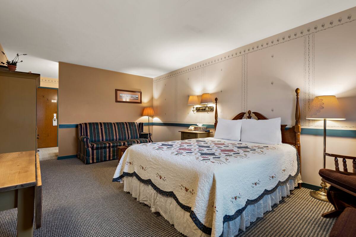 A hotel room with a large bed, a sofa, a desk, and a chair.