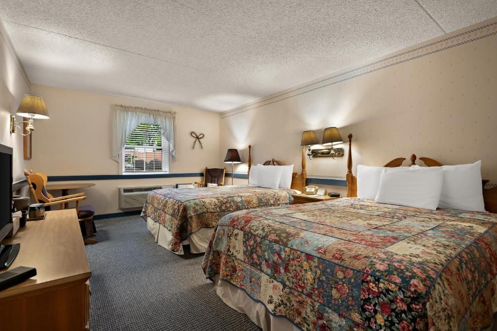 A hotel room with two beds, a desk with a chair, a television, and a window with blinds.