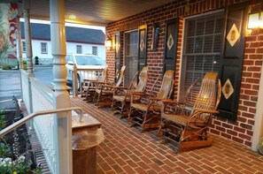 A brick building with a porch featuring wicker rocking chairs and a wooden bench.