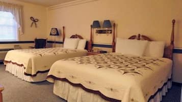 Habitación de hotel con dos camas individuales, una mesita de noche, una lámpara y un ventanal con cortinas.