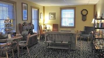 A room with a patterned carpet, a sofa, a chair, a table with a lamp, and a bookshelf.