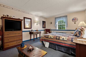 A bedroom with a bed, dresser, television, and a window with curtains.