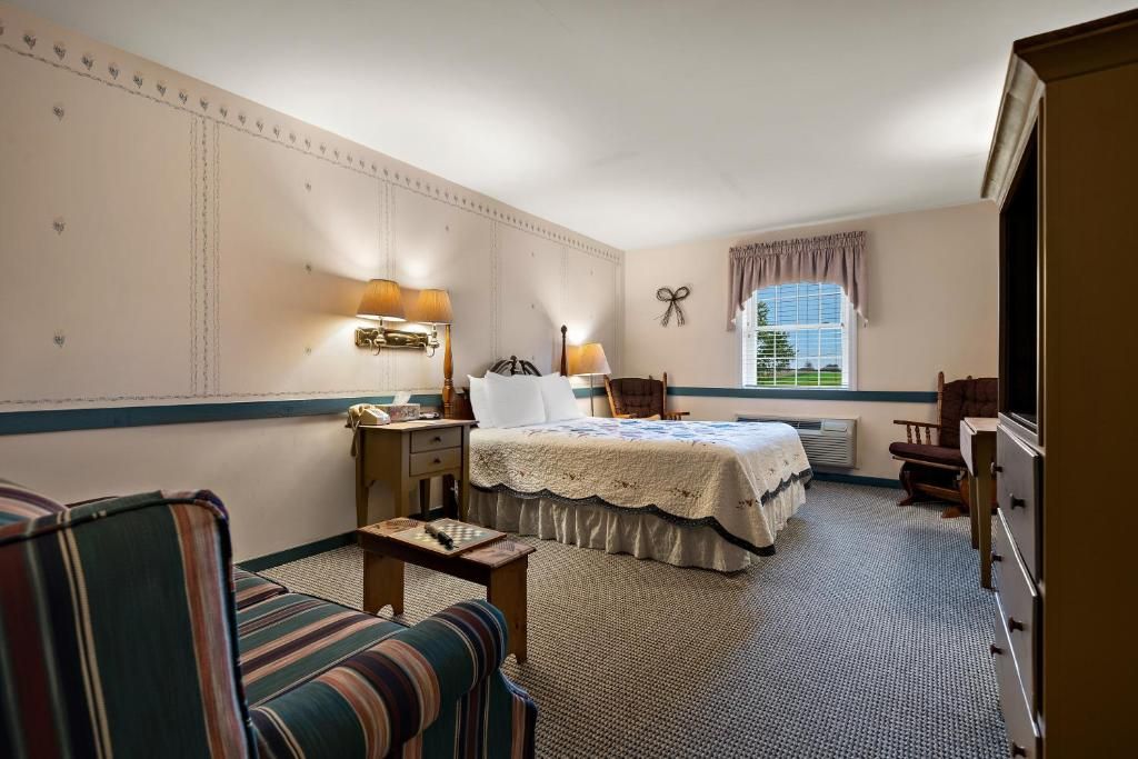 A hotel room with a bed, a desk, a chair, a dresser, and a window with curtains.