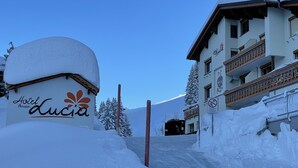 Entrada de un hotel cubierta de nieve con una estructura abovedada que dice 'Hotel Pension Lucia'.