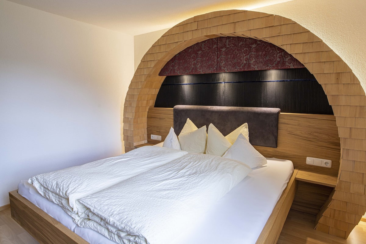 A bedroom with a wooden headboard, a bed with white bedding, and a small bedside table.