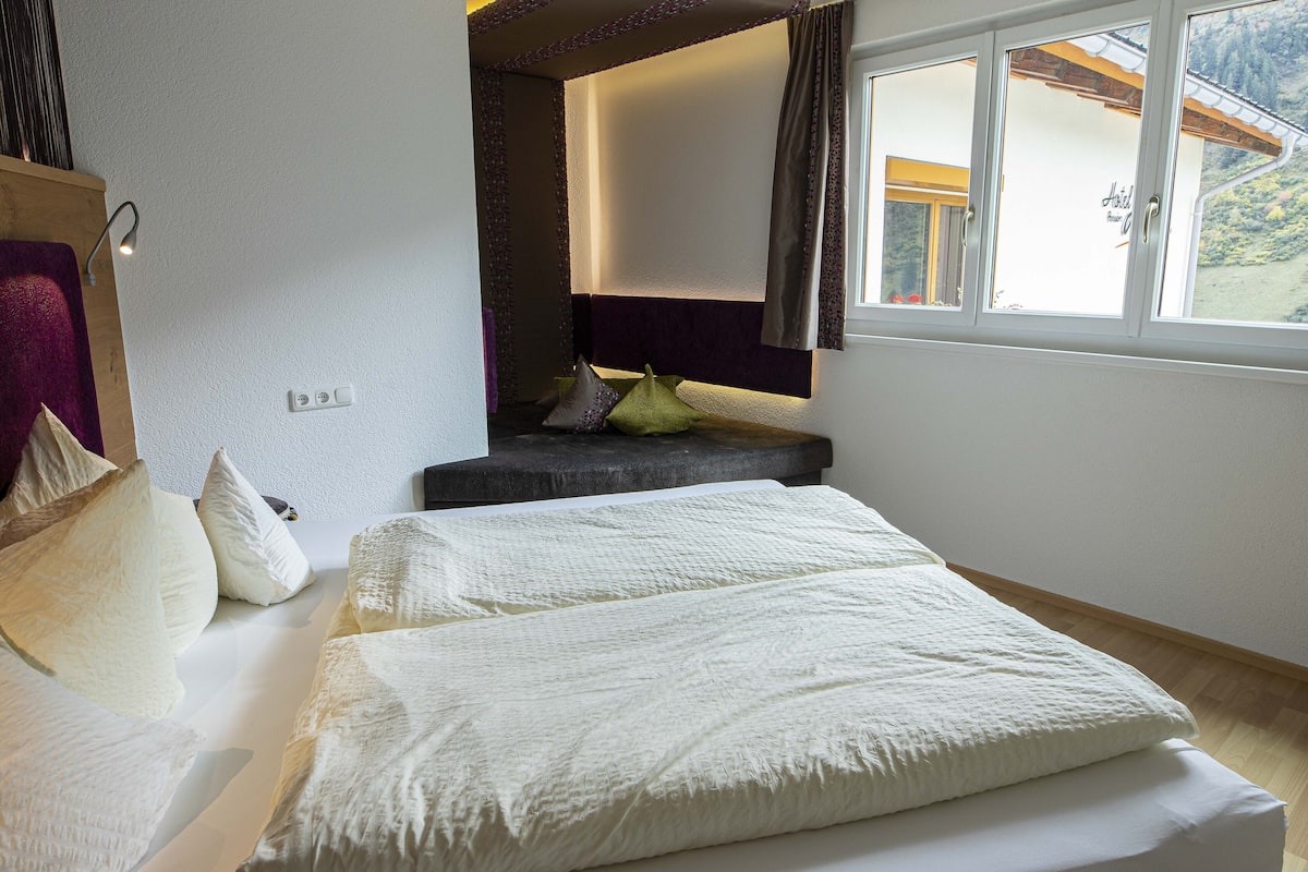 A bedroom with a bed, pillows, a window, and a view of a mountain.