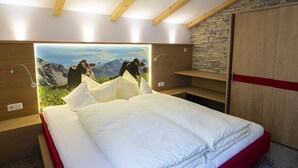 Un dormitorio con cama, cabecero de madera, pared de piedra y un mural con vista a la montaña.