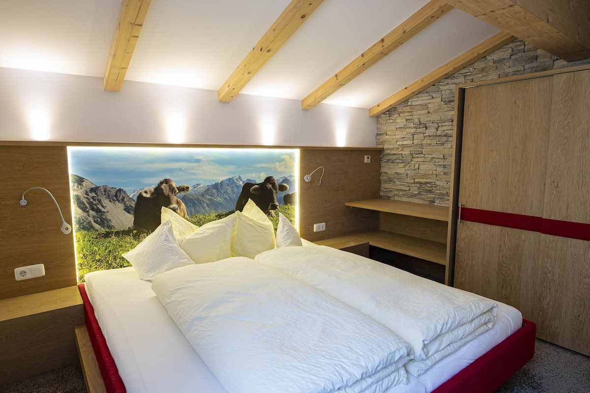 A bedroom with a bed, wooden headboard, stone wall, and a mountain view mural.