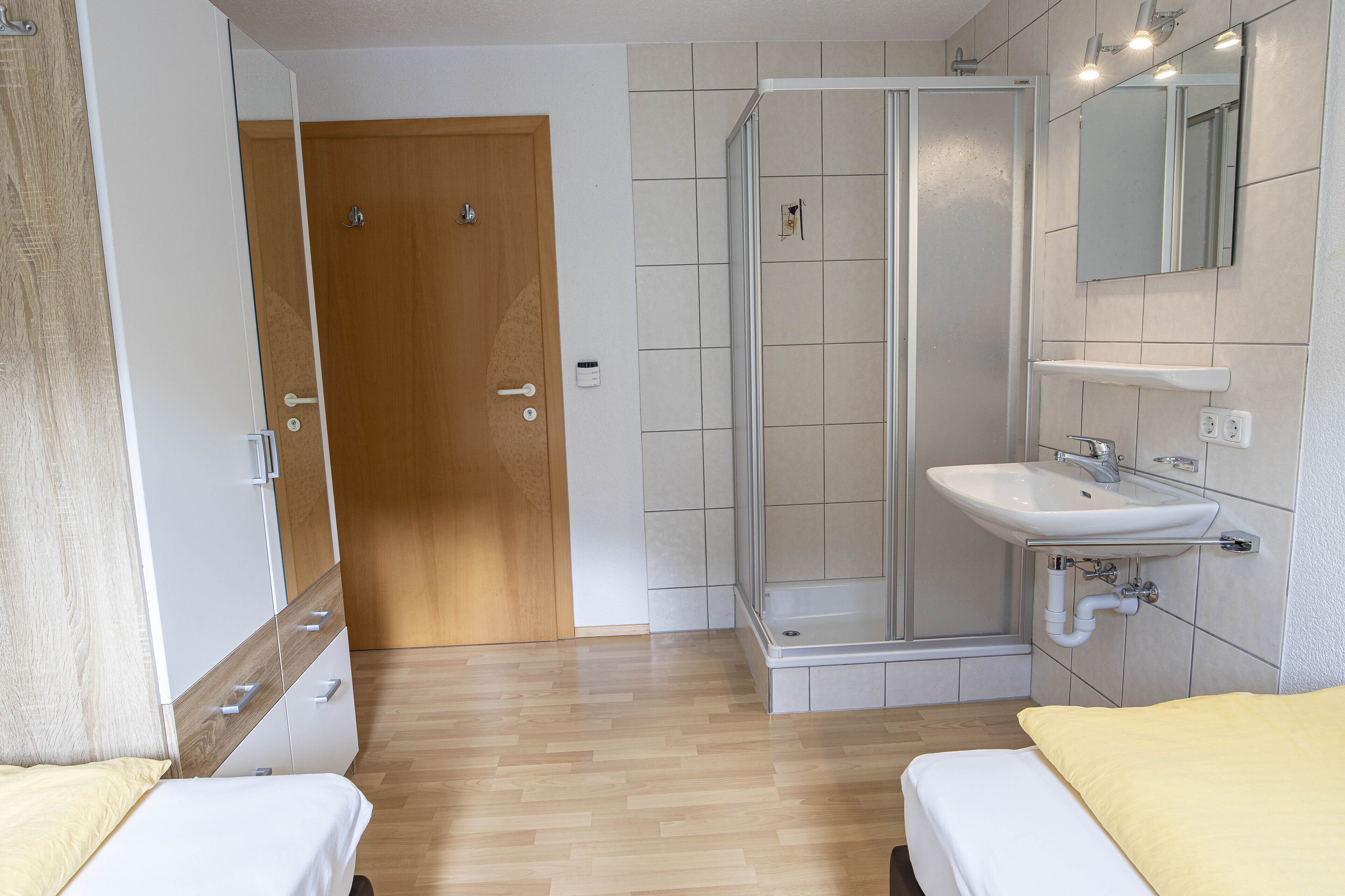 A hotel room with a wooden door, a shower area, a sink, and two beds with yellow bedding.