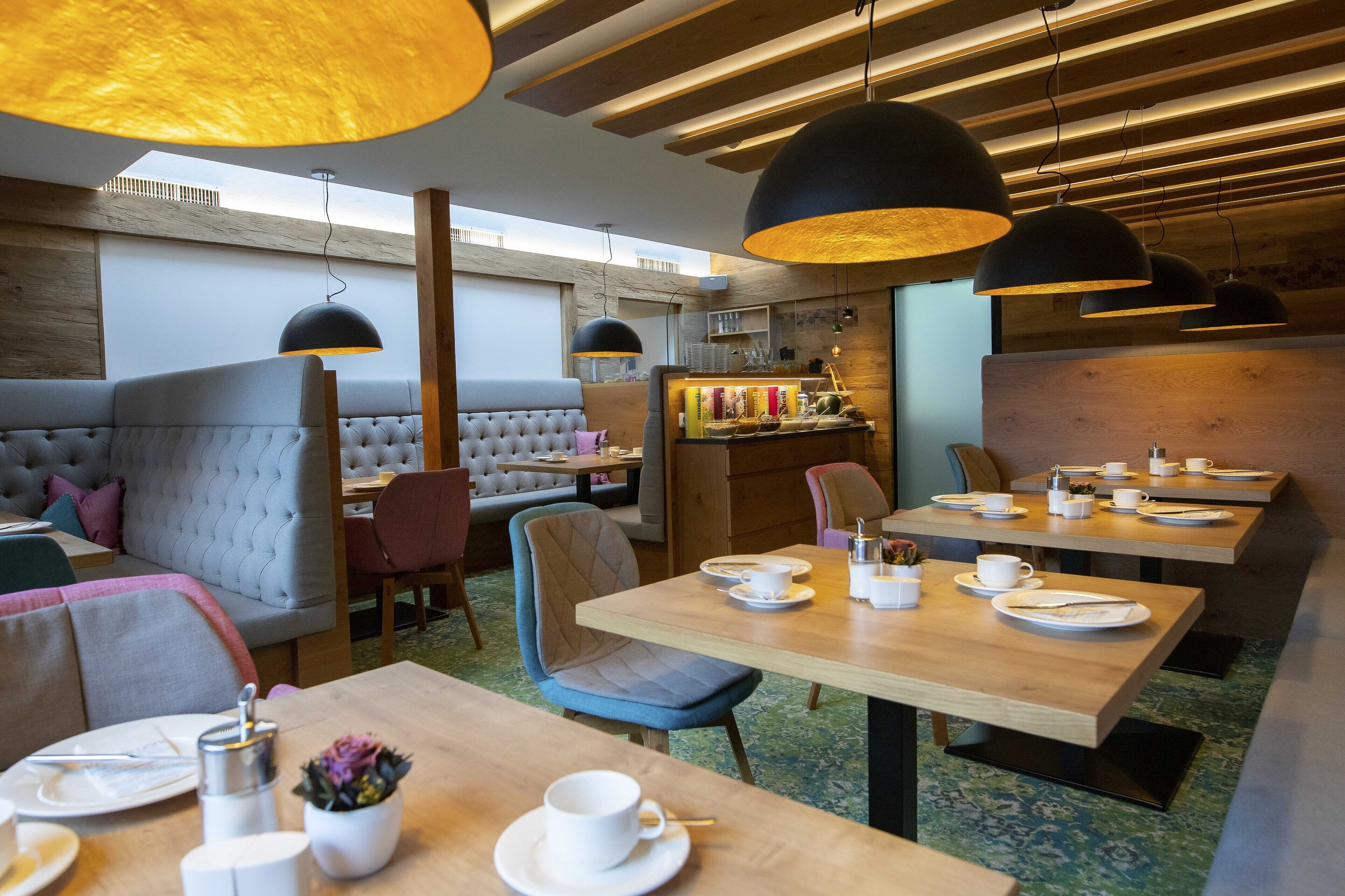 A modern restaurant with wooden tables, cushioned seating, pendant lighting, and a visible bar area.