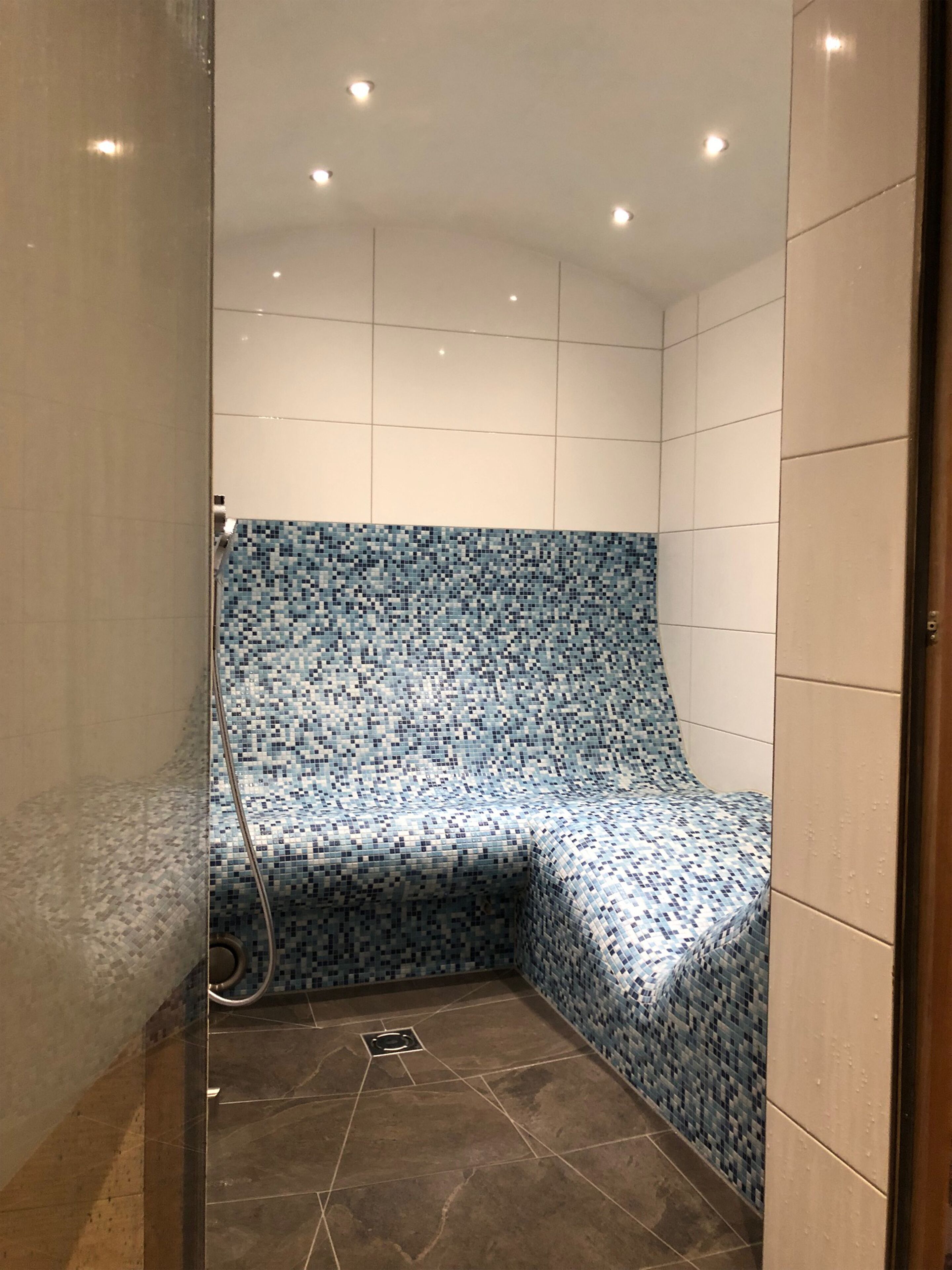Zona de ducha con pared y suelo de azulejos, un cabezal de ducha y desagüe.