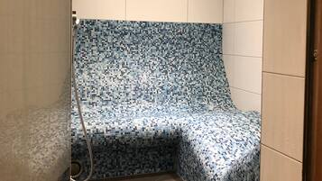 Zona de ducha con pared y suelo de azulejos, un cabezal de ducha y desagüe.