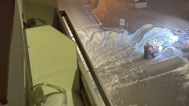 A snowy outdoor scene with a person standing near a vehicle, possibly a snowplow, and a no parking sign visible. - Hotel Lucia (Damüls)