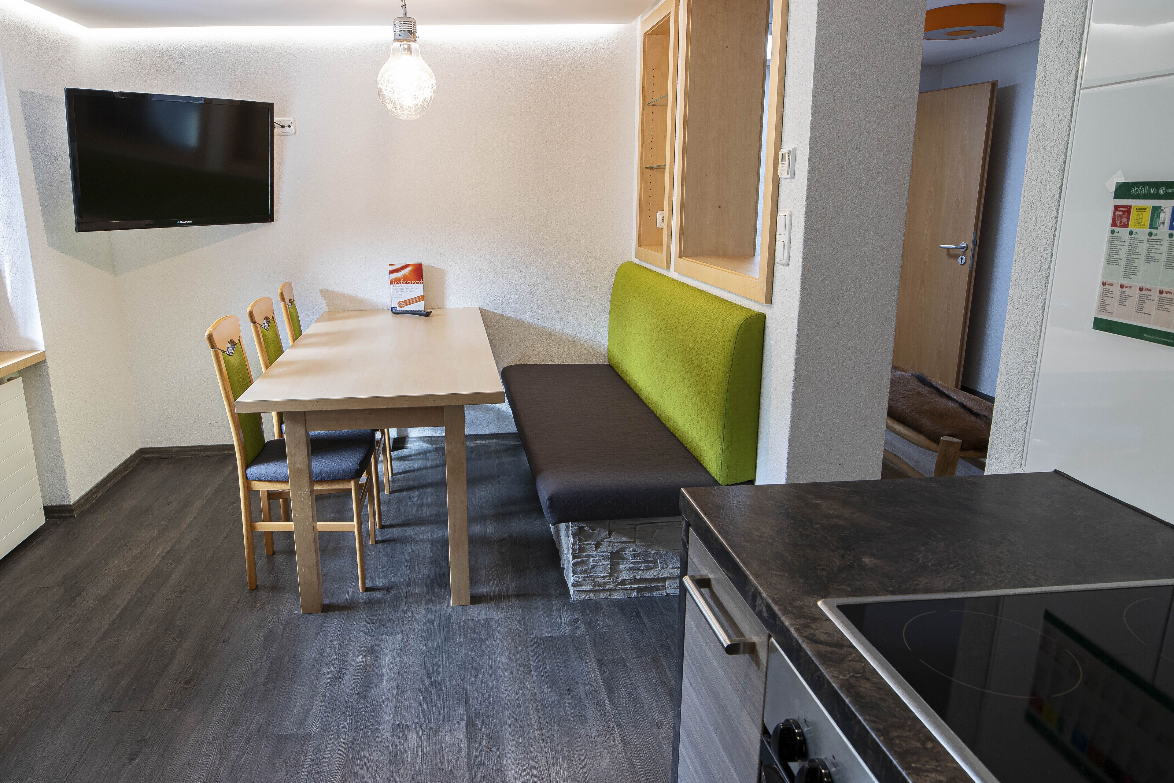 A compact kitchen with a built-in stove, a dining table with chairs, and a bench.