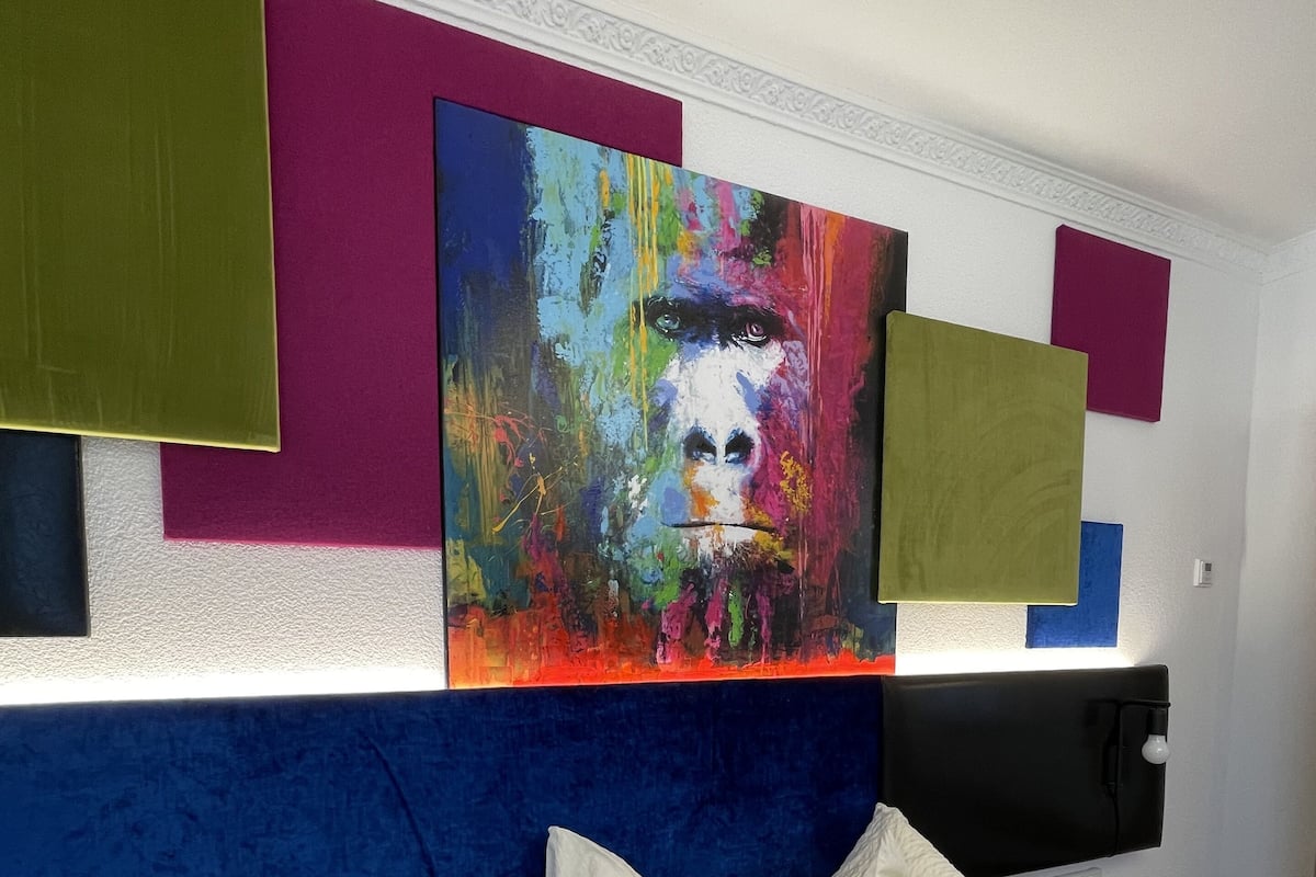 A modern hotel room with a large bed, white pillows, and a colorful abstract painting on the wall.