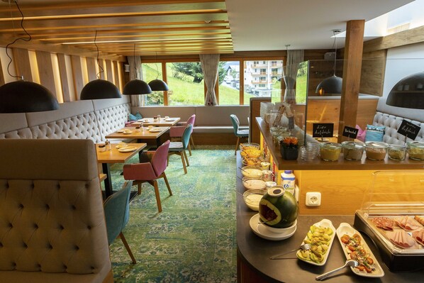 A hotel dining area with a buffet, seating arrangements, and a view of the outdoors. - Hotel Lucia (Damüls)
