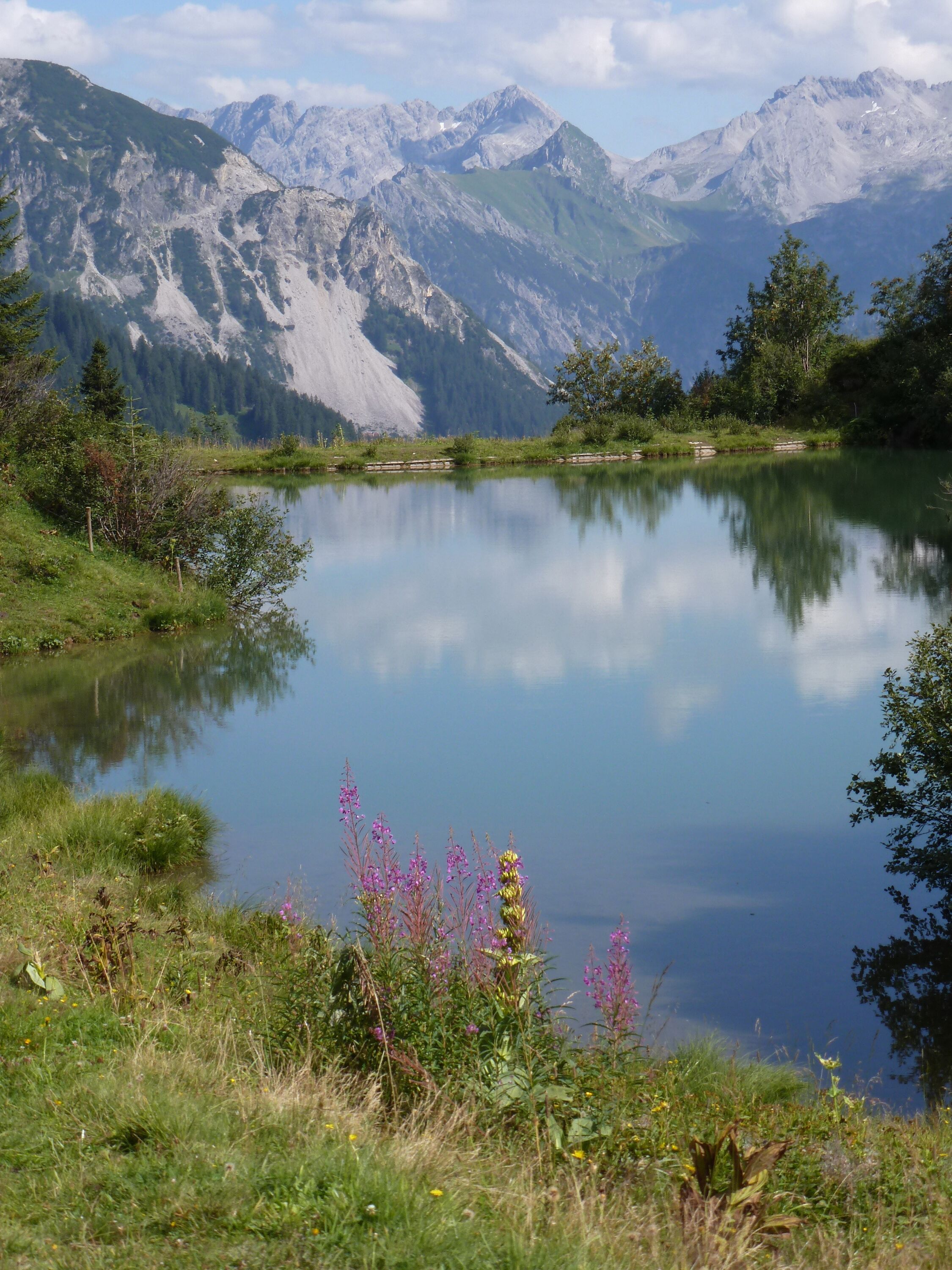 A tranquil lake surrounded by mountains, with clear reflections and lush greenery.