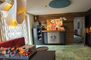 A modern living room with a fireplace, a red sofa, a wooden accent wall, and a decorative painting. - Hotel Lucia (Damüls)