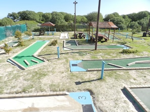 Ein Minigolfplatz mit nummerierten Bahnen, grünen und blauen Spielflächen und Picknicktischen.