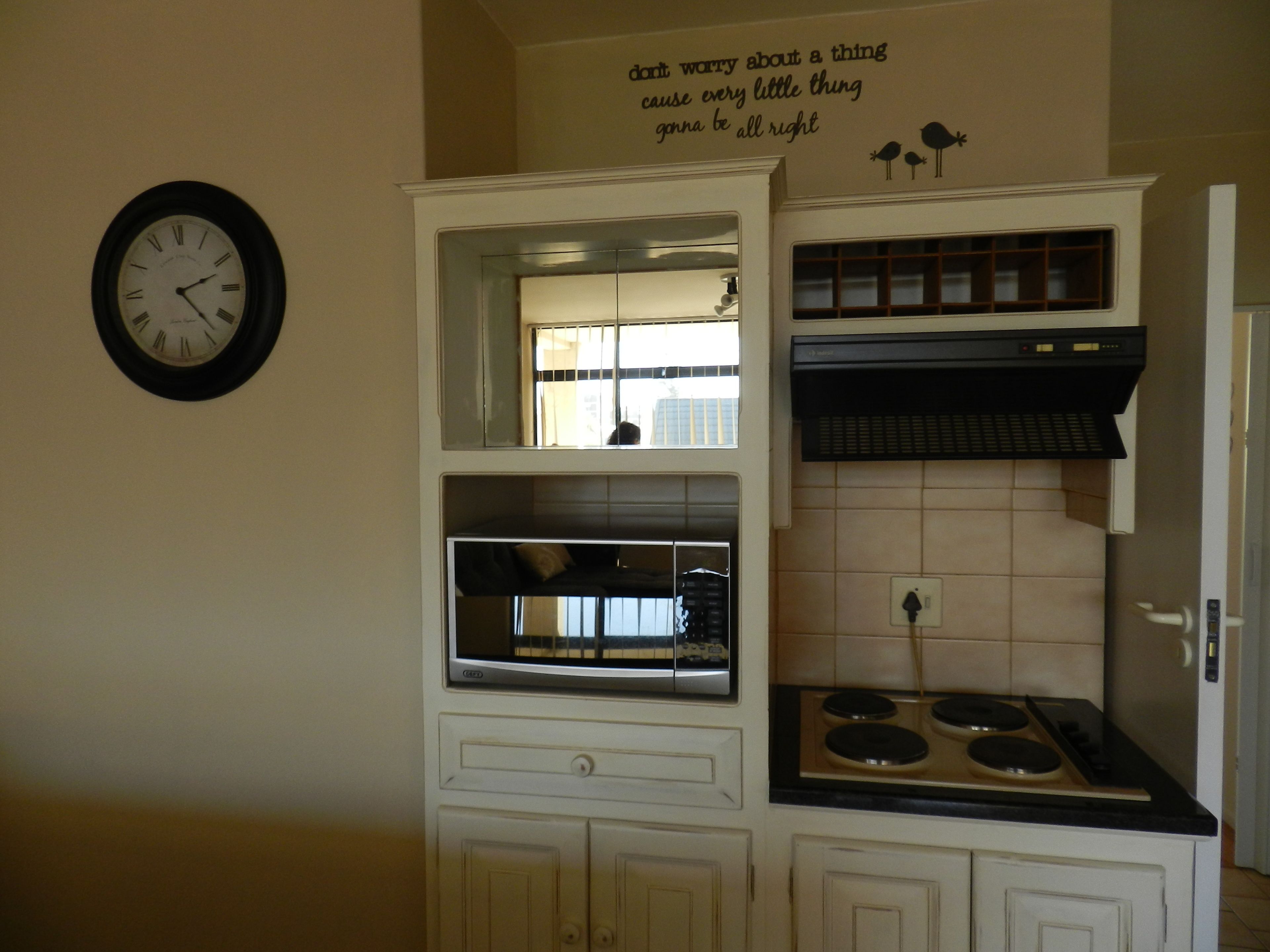Une cuisine équipée d’un four, d’un micro-ondes et d’une cuisinière encastrés. Il y a une horloge au mur et un panneau avec un message.
