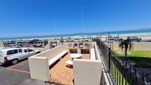 En tagterrasse med siddeområde, udsigt til stranden og en parkeringsplads med biler.