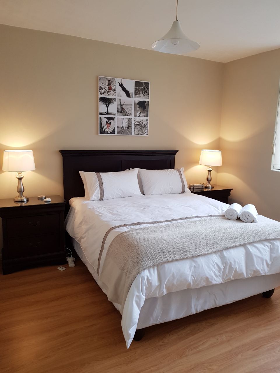 A neatly made bed with white bedding and two bedside lamps, a wall-mounted picture, and a ceiling fan.