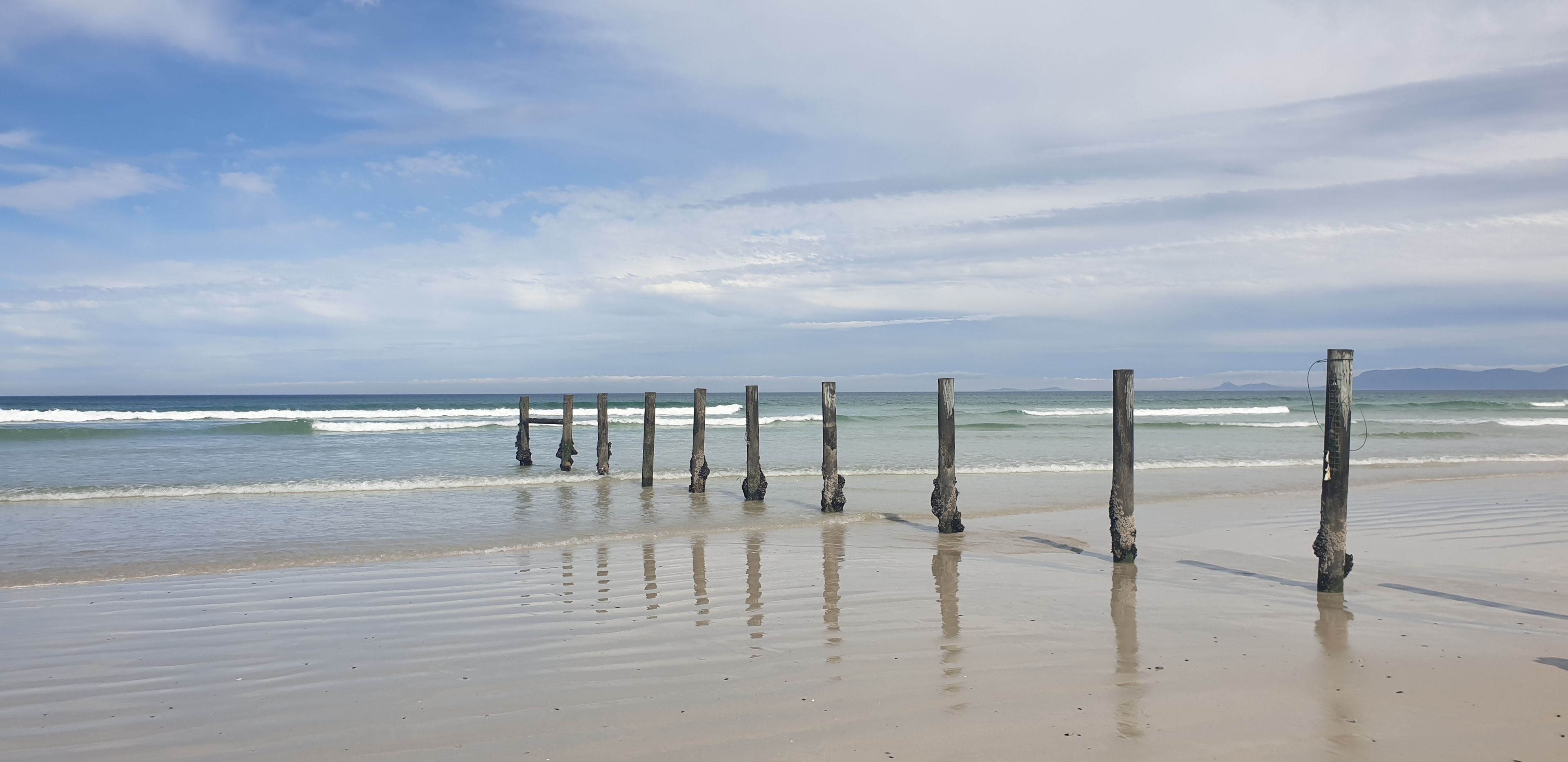 Une plage avec des poteaux en bois et des vagues calmes.