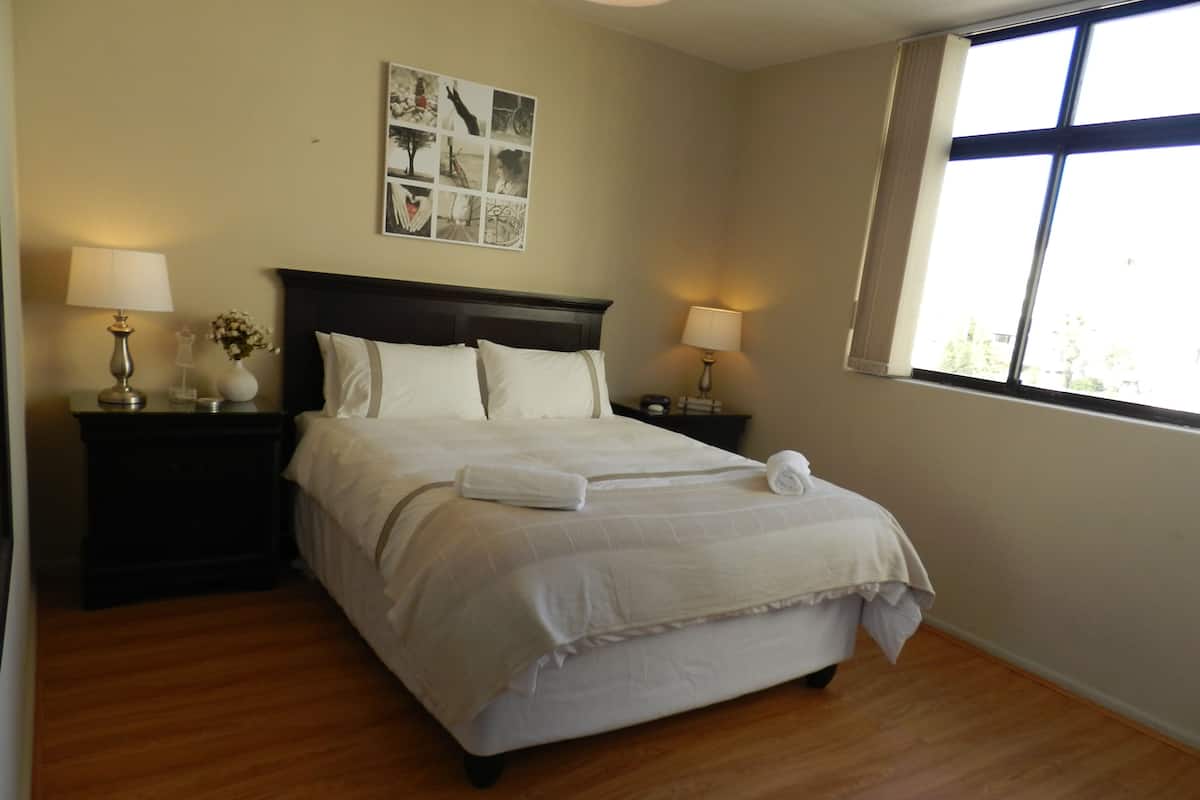 A neatly made bed with white linens, two bedside tables with lamps, and a wall art piece above the bed.
