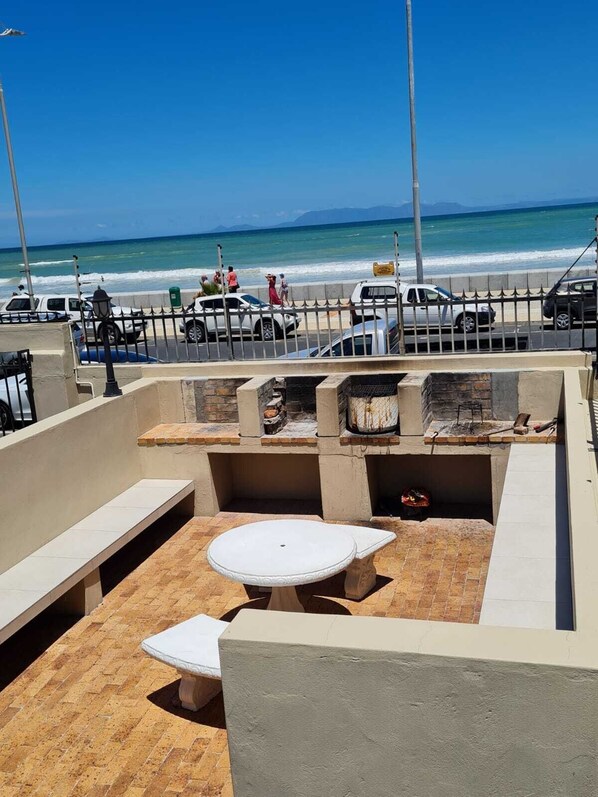 An outdoor seating area with a table and benches, overlooking a beach with cars parked along the shore.