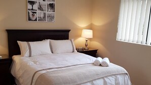 En pænt redt seng med mørkt sengegavl, et natbord med lampe og et billed på væggen.