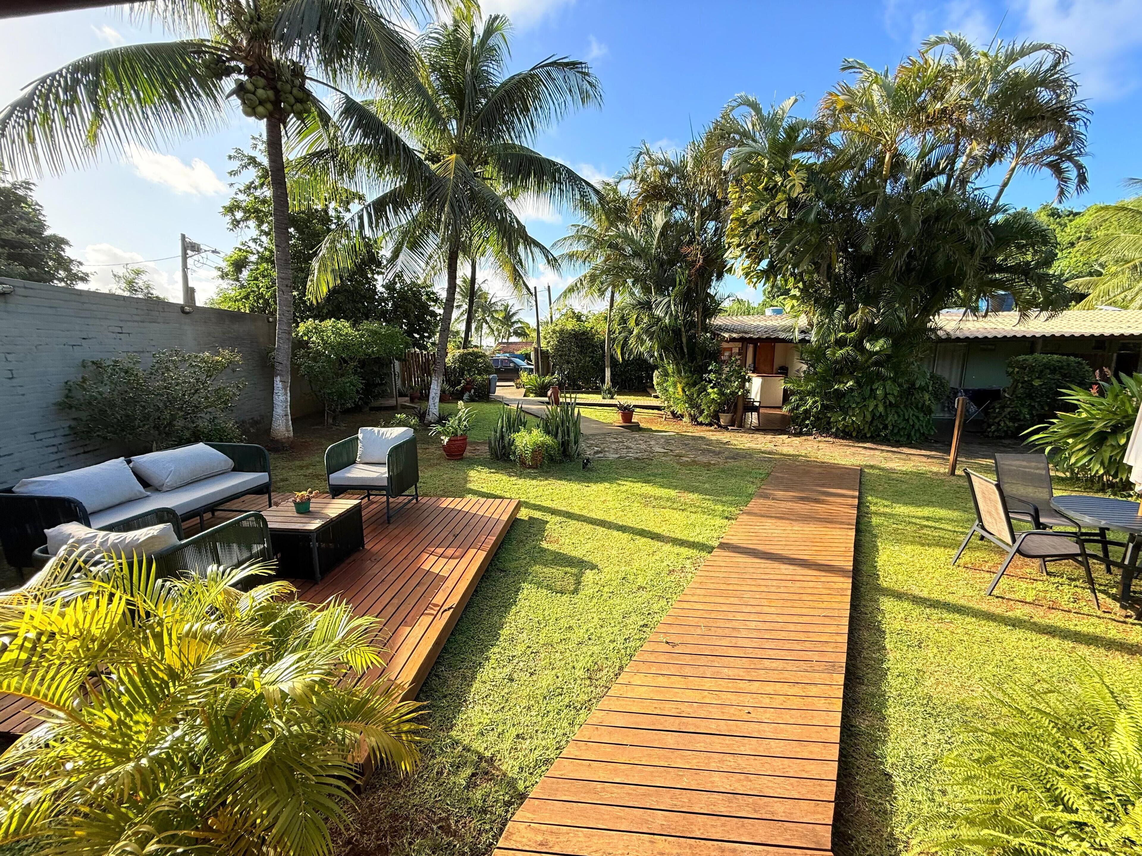 A backyard with a wooden deck, outdoor furniture, and lush greenery including palm trees.