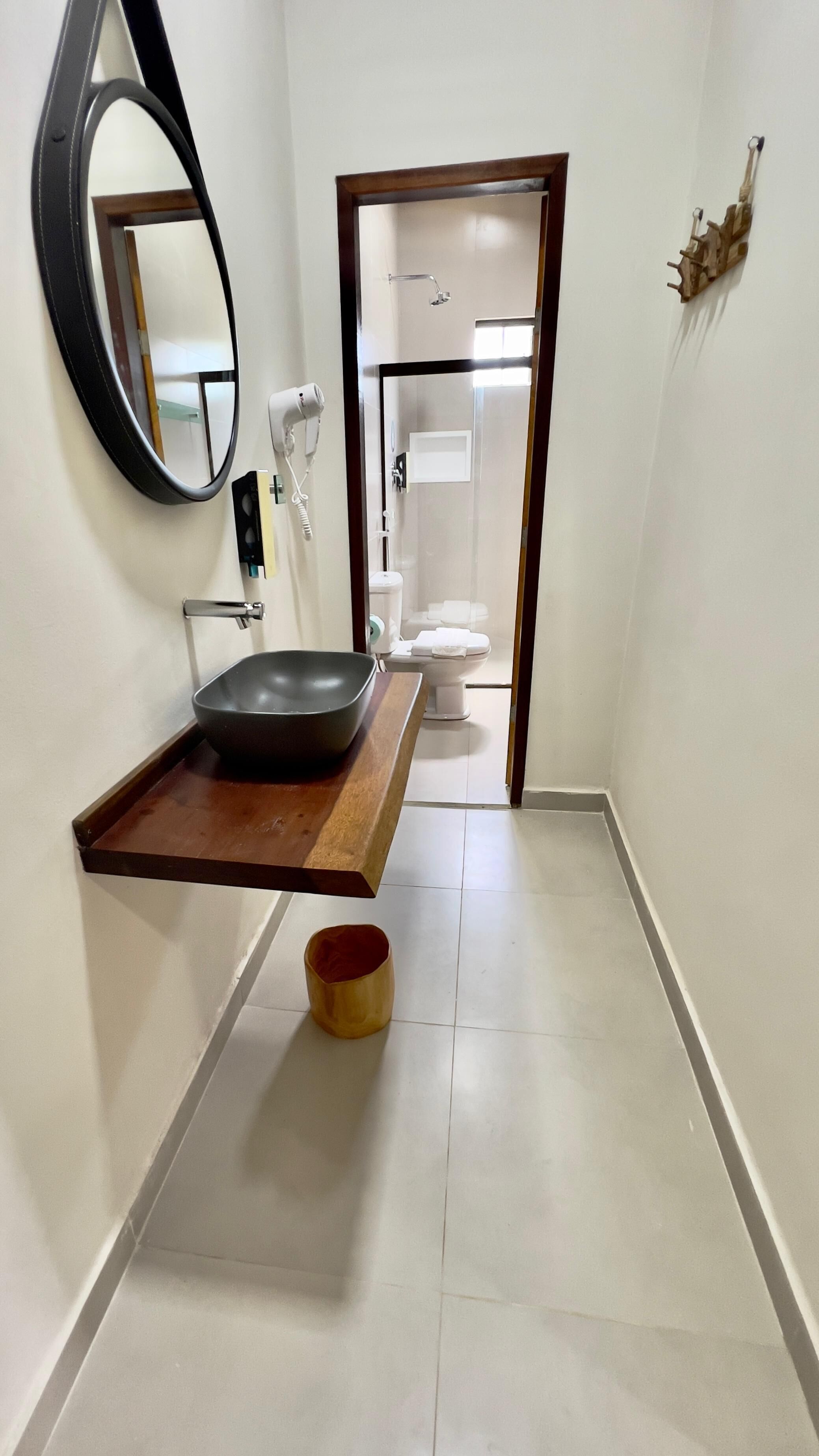 Une salle de bain avec un lavabo noir posé sur un plateau en bois, des toilettes blanches et un miroir au mur.