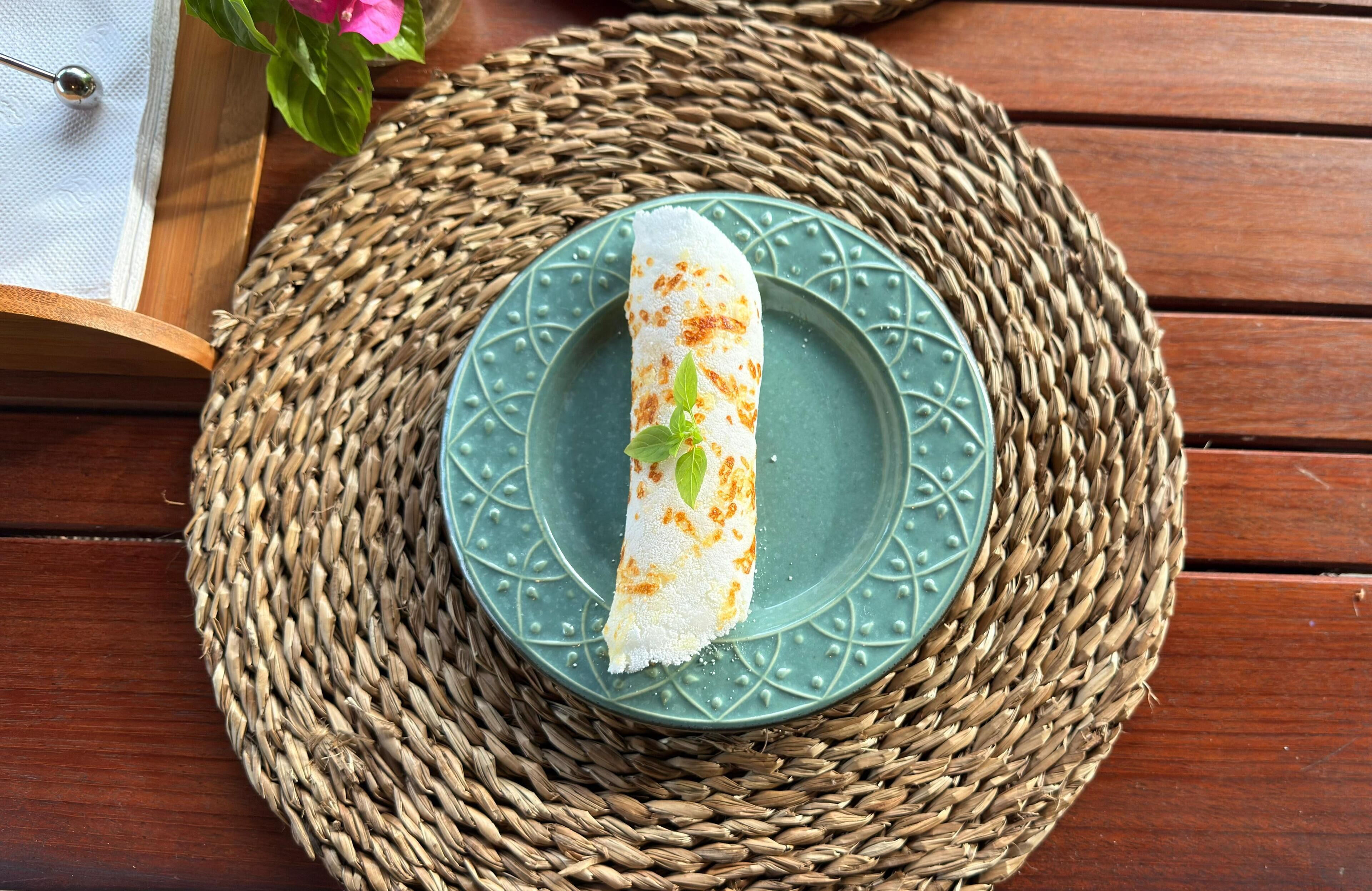 A rolled crepe on a green plate with a woven placemat.