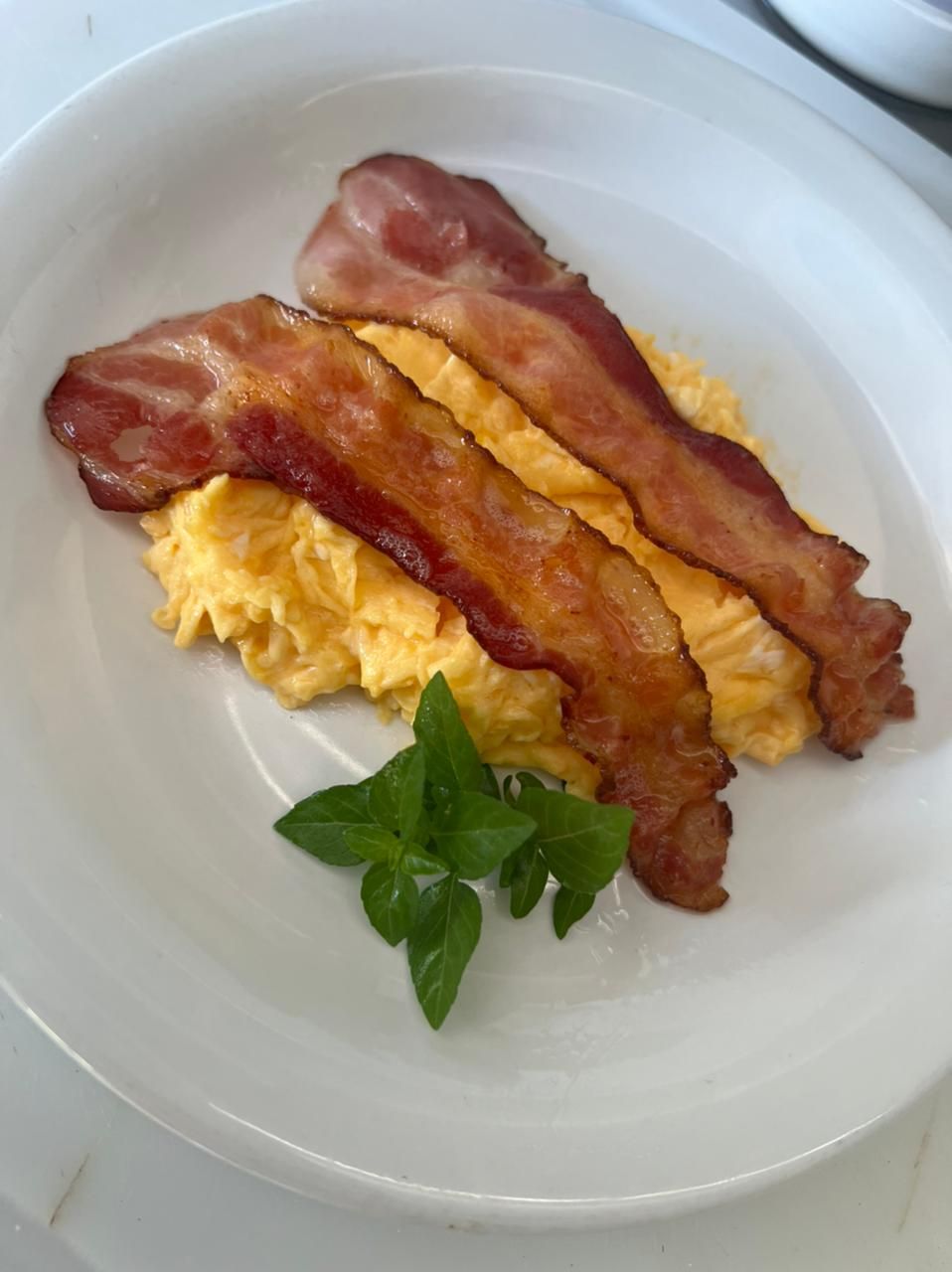 A plate with scrambled eggs and bacon strips, garnished with a basil leaf.