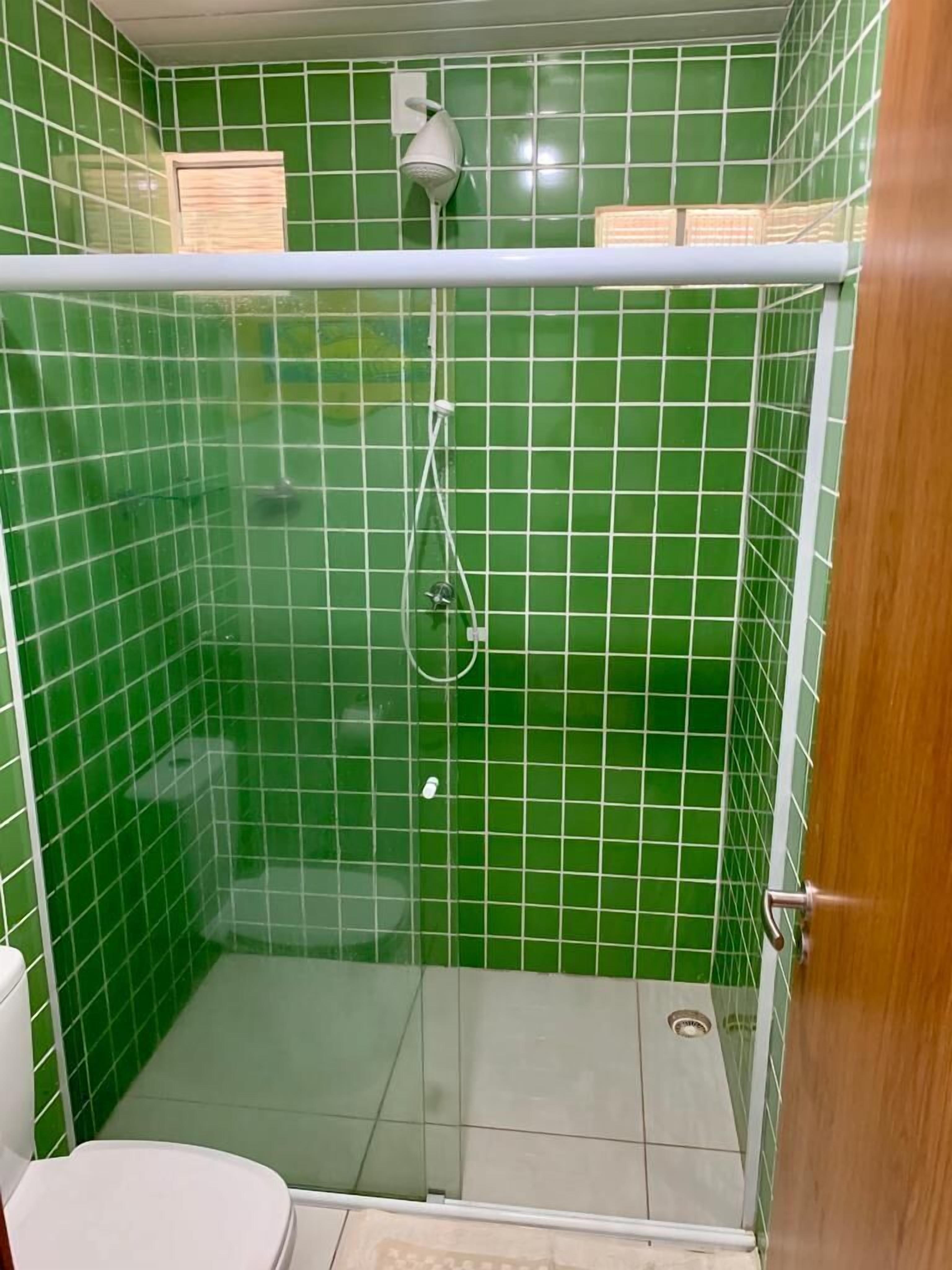 Ein kleiner, abgeschlossener Duschbereich mit grünen Fliesenwänden und einer Glastür.