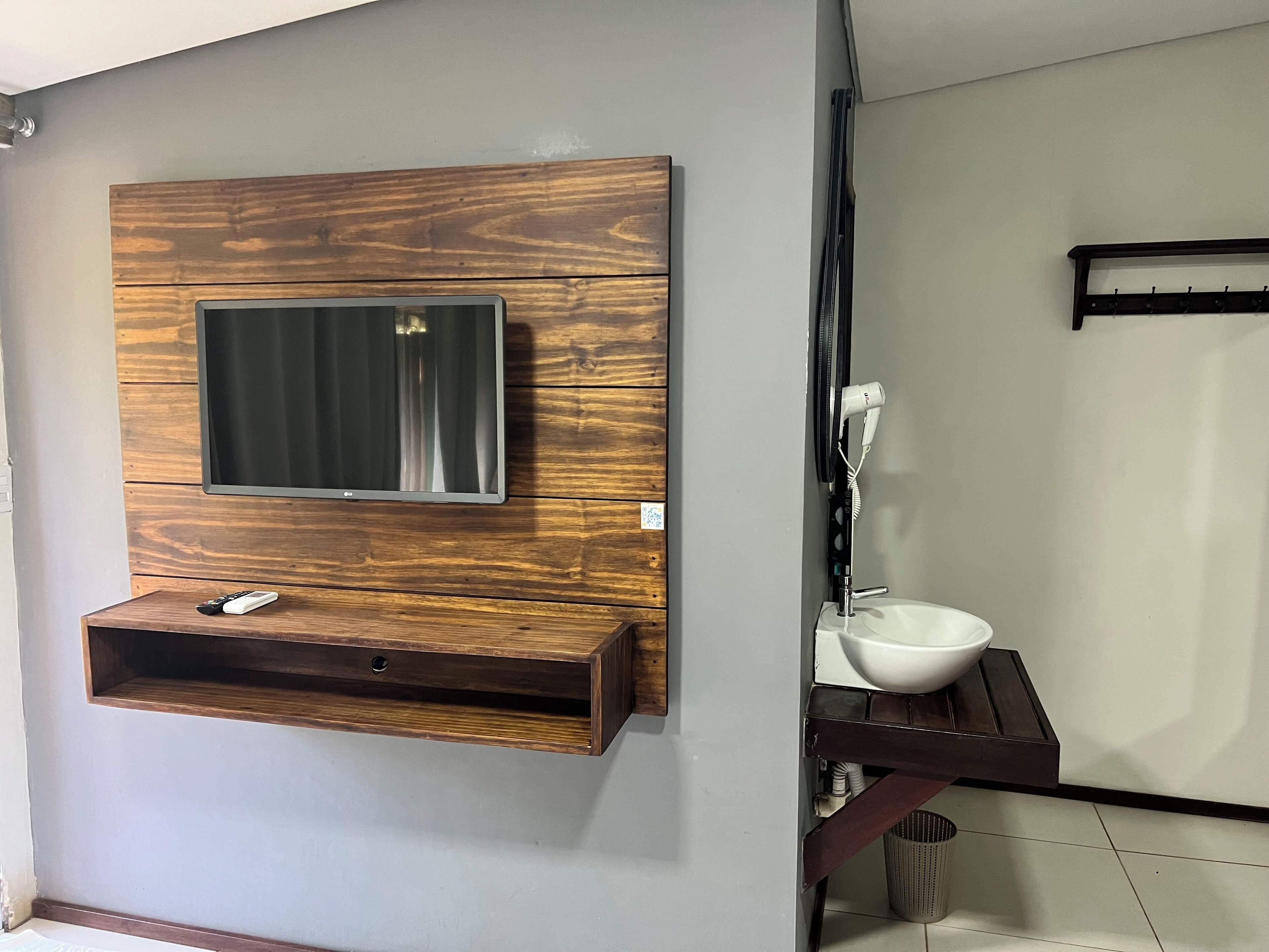 Un baño con tocador de madera, espejo, lavamanos y perchero para toallas.