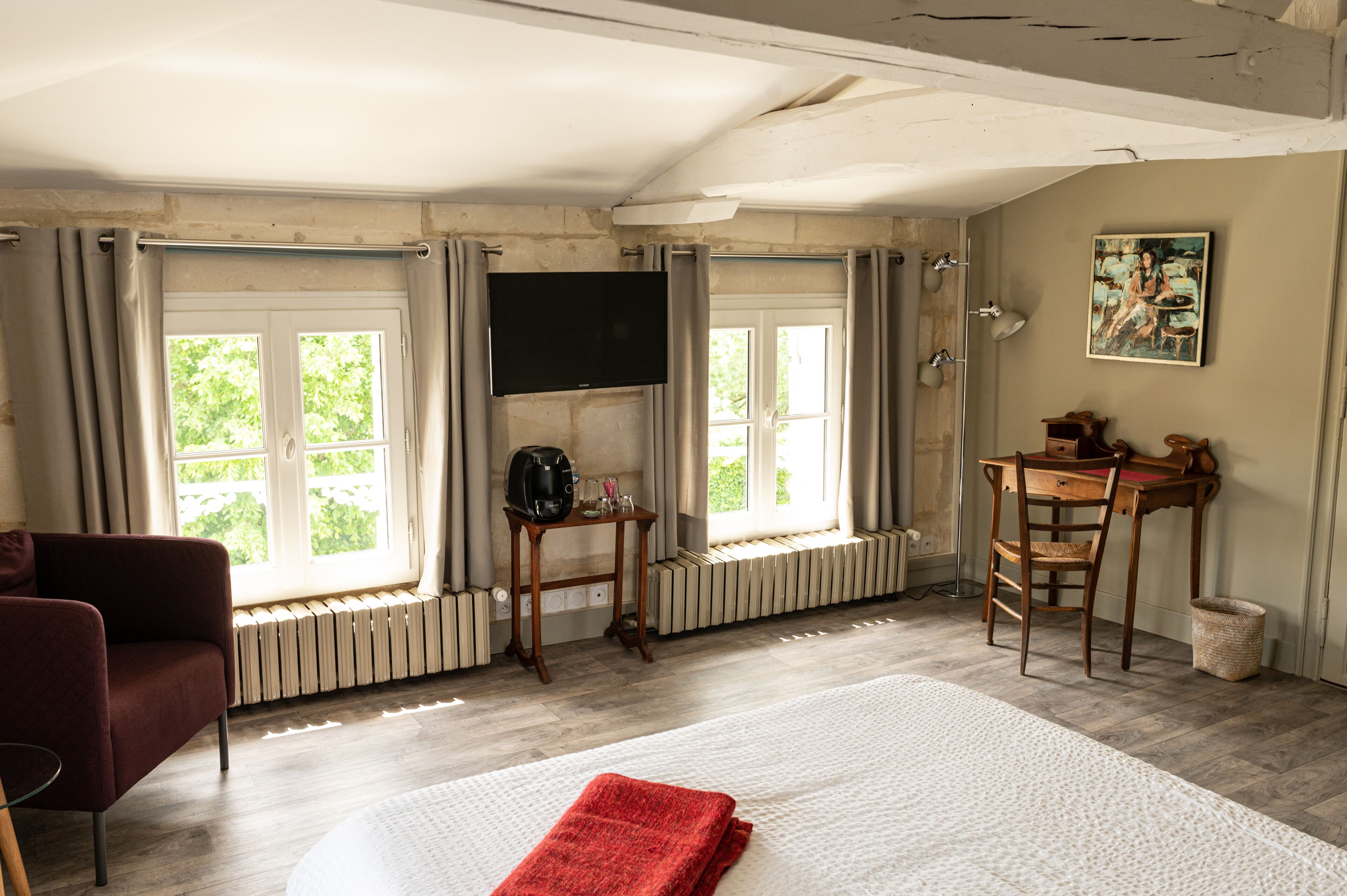 A room with a bed, a TV mounted on the wall, a wooden table with chairs, and a window with curtains.