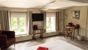 A room with a bed, a TV mounted on the wall, a wooden table with chairs, and a window with curtains.