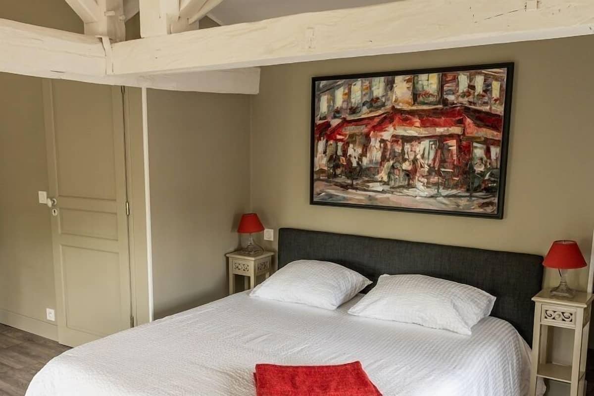 Une chambre à coucher avec un grand lit, deux tables de chevet avec des lampes, une porte et un tableau au mur.