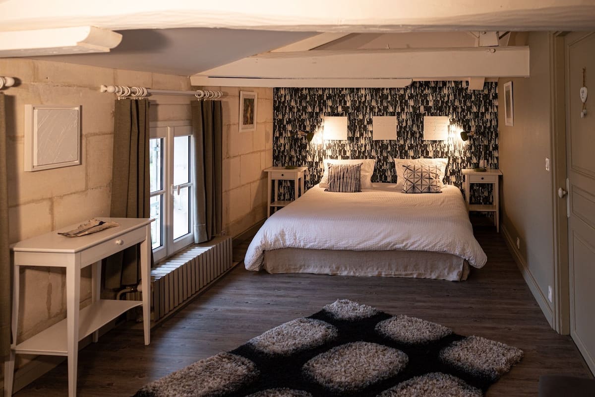 Une chambre à coucher avec un grand lit, deux lampes de chevet, un radiateur, un bureau et un tapis à motifs.