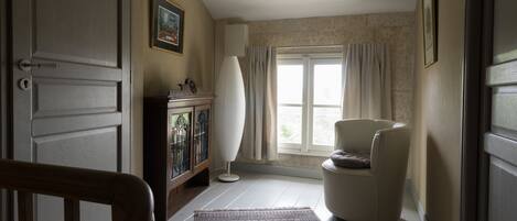 Un pasillo con un suelo estampado, una silla blanca, un mueble con puertas de cristal y una ventana con cortinas.
