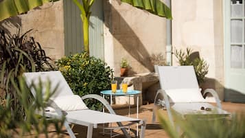 Deux fauteuils blancs avec des coussins, une petite table avec deux verres de jus d’orange et une plante en pot.