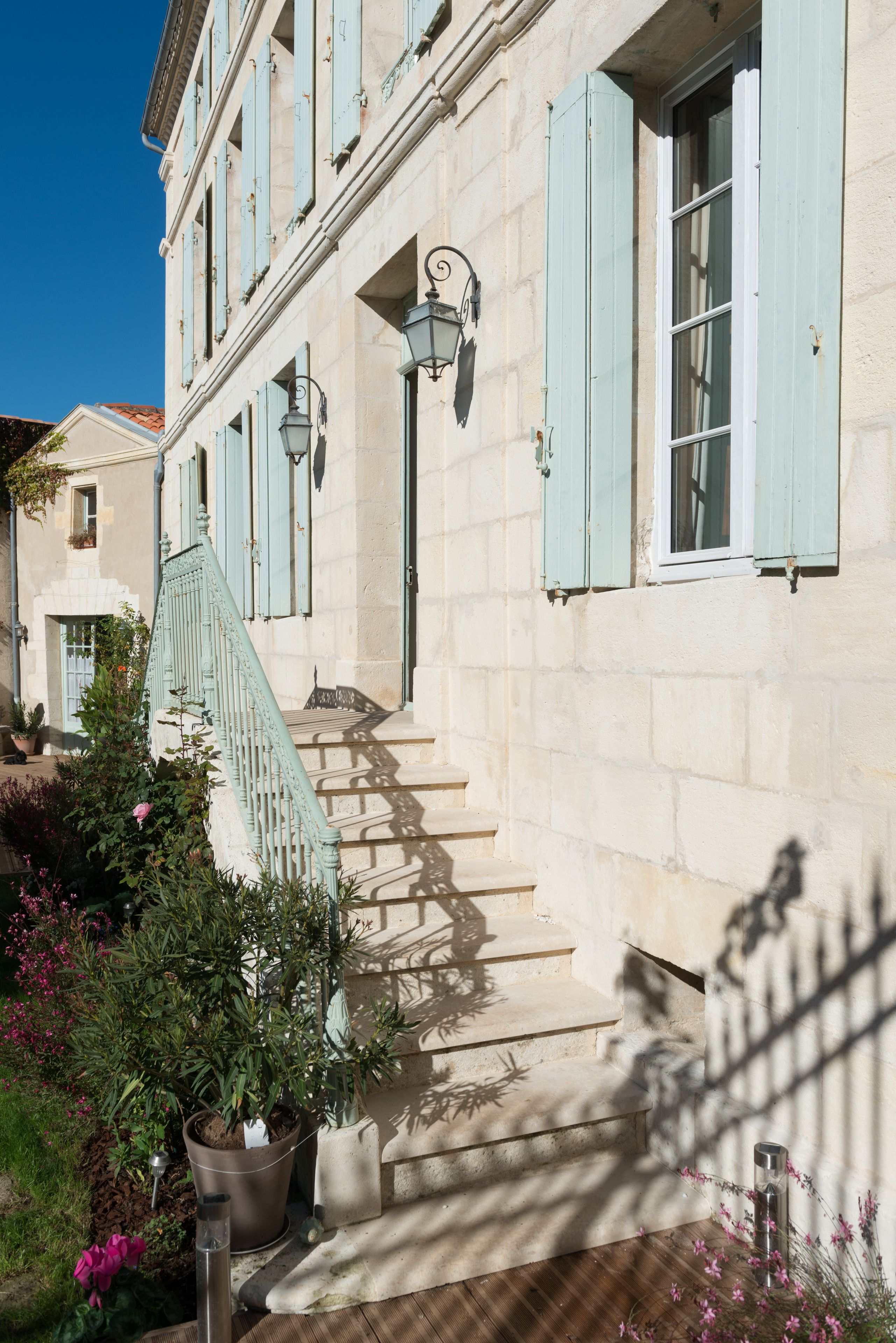 A building with a stone facade, a staircase with a green railing, and a potted plant in the foreground.