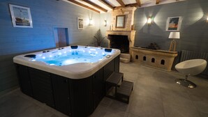 Un baño moderno con jacuzzi, vigas de madera, chimenea y una silla blanca.