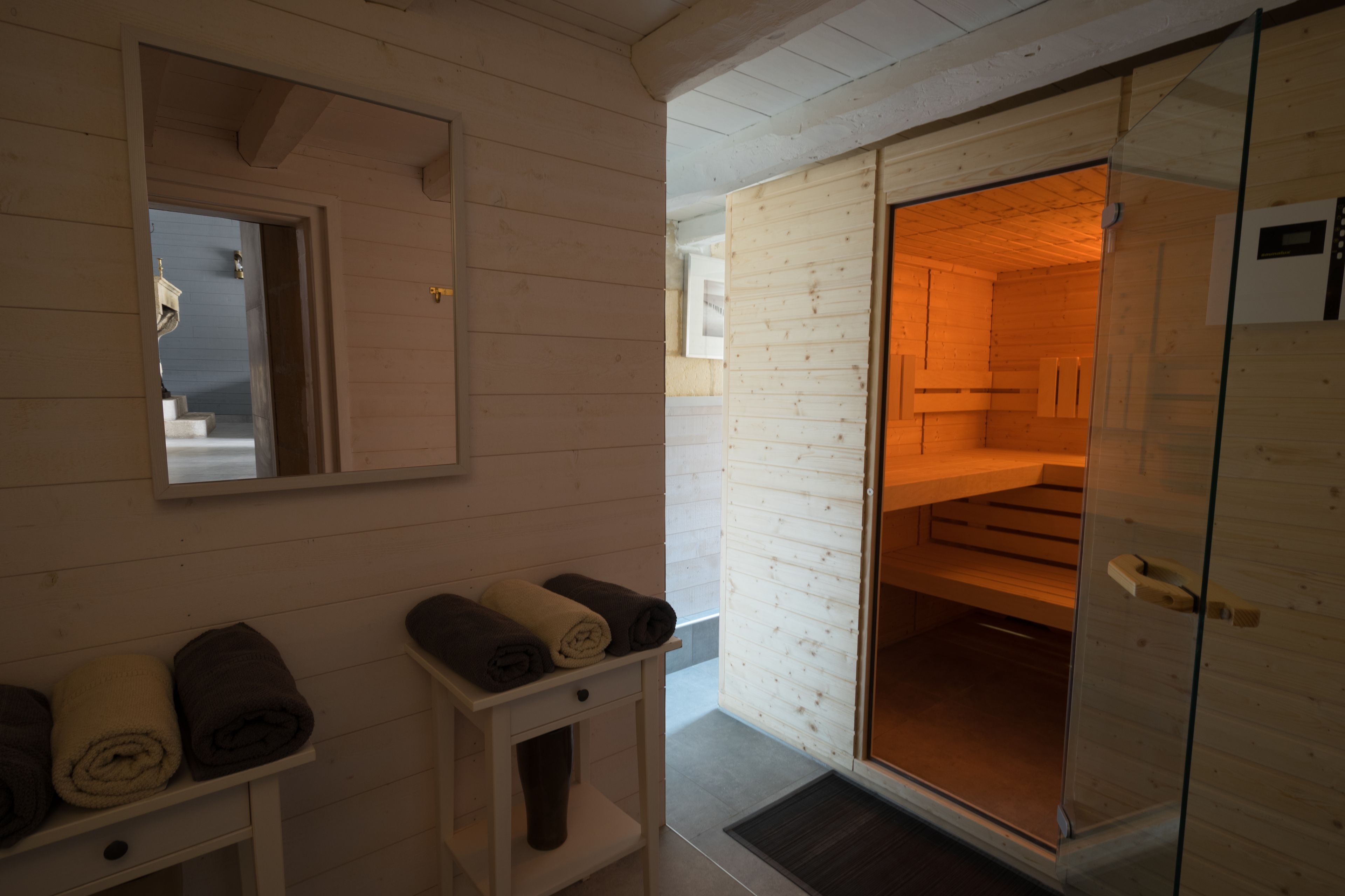 Un interior de madera con un espejo, una mesita con toallas y una puerta corredera que da a otra habitación.