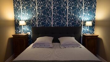 A neatly made bed with a striped bedspread and two pillows, flanked by two bedside tables with lamps, against a wall with a tree pattern wallpaper.