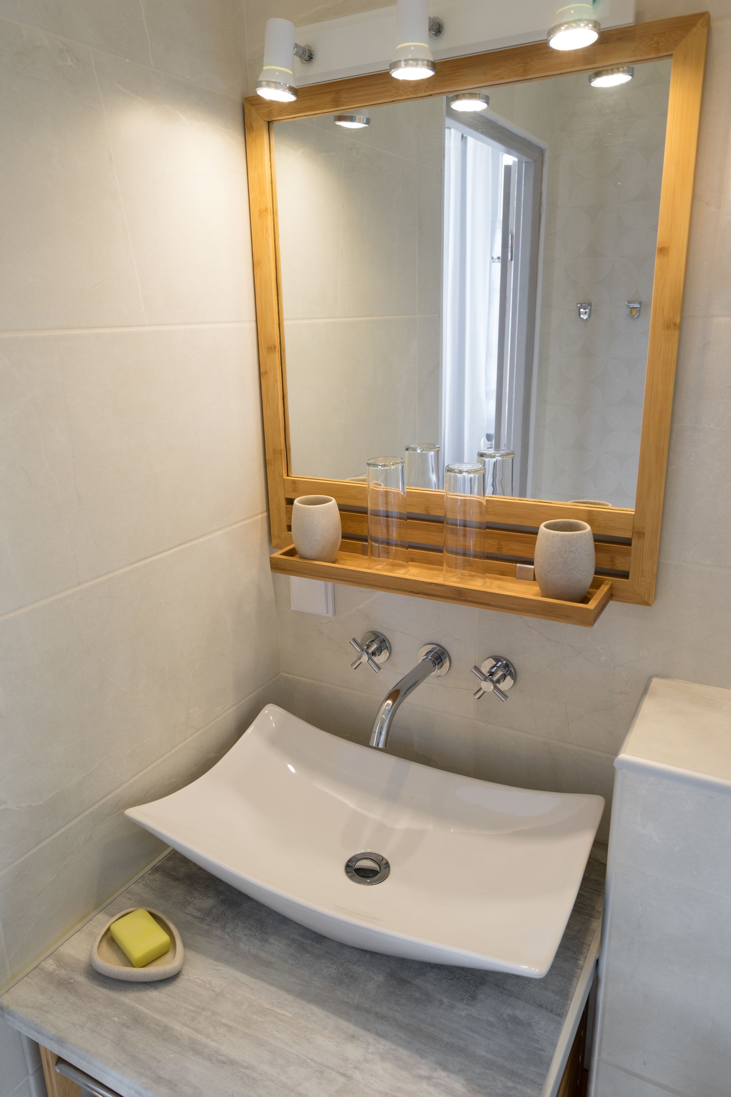 A bathroom with a white sink, a wooden shelf with toiletries, and a mirror with lights.