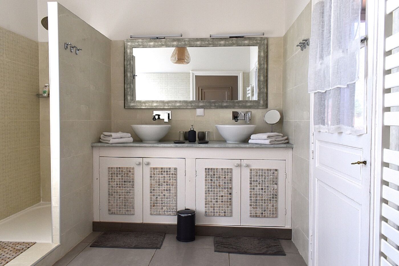 Un baño con un espejo grande, dos lavamanos, ducha y retrete.